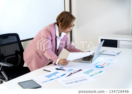 Senior female executive is standing looking at documents and computers Senior female executive is standing looking at documents and computers 134728446