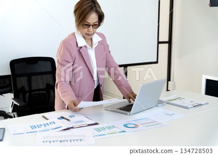 Senior female executive is standing looking at documents and computers 134728503