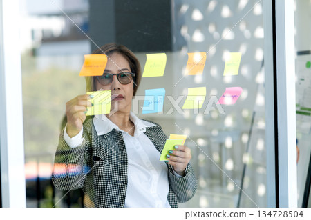 Senior business woman is looking at and writing messages on sticky notes 134728504
