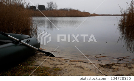 A rubber boat with an oar stands on the shore of a lake in autumn.  134728530