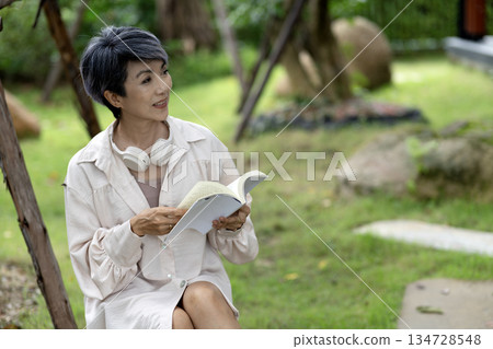 elderly woman sits on a rock reading a book in the garden enjoying 134728548