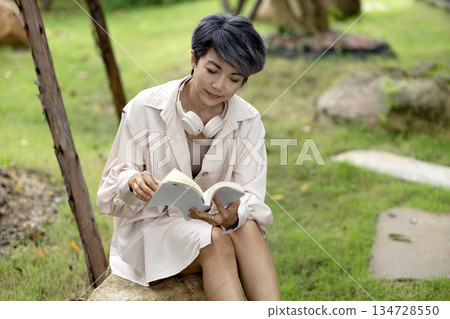 elderly woman sits on a rock reading a book in the garden enjoying 134728550