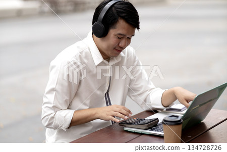man wearing headphones while typing data on a laptop for communication or entertainment 134728726