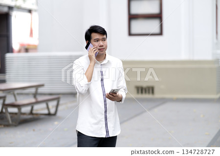 Businessman in casual clothes talking on the phone walking outdoors Businessman in casual clothes talking on the phone walking outdoors 134728727