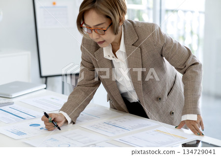 Senior female executive is standing looking at documents and computers arranged 134729041