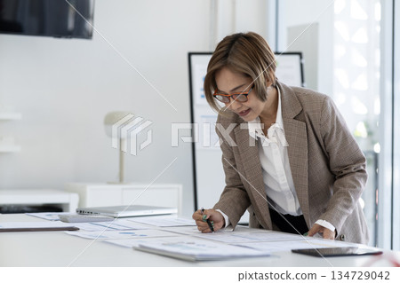 Senior female executive is standing looking at documents and computers arranged Senior female executive is standing looking at documents and computers arranged 134729042