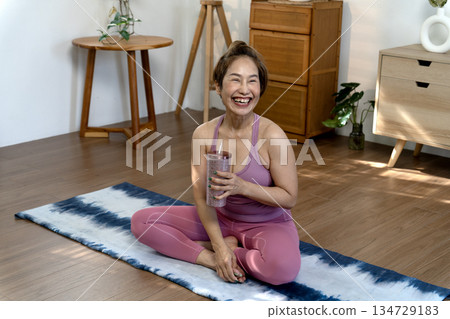 Smile woman in yoga dress sit on yoga mate Drink water to relax Smile woman in yoga dress sit on yoga mate Drink water to relax 134729183