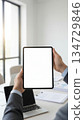 Tablet with a blank screen held in a modern office. Concept of business, remote work, digital productivity, technology, and professional workplace. Ideal for presentations, advertising, and stock illu 134729846