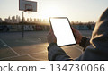 Tablet with a blank white screen on a basketball court. Concept of sports technology, coaching, digital tools, and professional performance tracking. Commercial stock-ready. 134730066