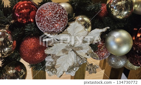 Peppermint-striped plush ornaments hang among red and gold baubles on green pine branches, capturing festive warmth and playful charm in a vibrant Christmas tree close-up. 134730772