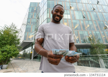 African American man holding money dollar bills on urban street in city. Businessman guy counting paper currency money outdoors near office bank building. Man holding cash. Finance economy banking African American man holding money dollar bills on urban street in city. Businessman guy counting paper currency money outdoors near office bank building. Man holding cash. Finance economy banking 134731114