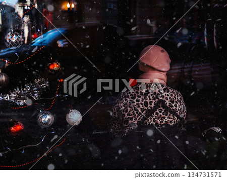 Urban winter mood. Unrecognizable person in trendy leopard print jacket and pink beret watching Christmas tree in a winter snowfall Snowflakes falling 134731571