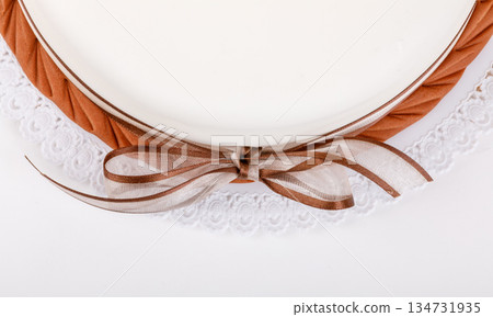 Close-up of an empty plate with a brown bow, decorative napkin and brown trim. Close-up of an empty plate with a brown bow, decorative napkin and brown trim. 134731935