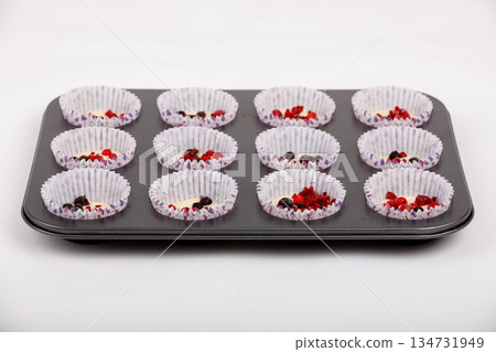 Tray of cupcake liners filled with batter and mixed berries ready for baking. Tray of cupcake liners filled with batter and mixed berries ready for baking. 134731949