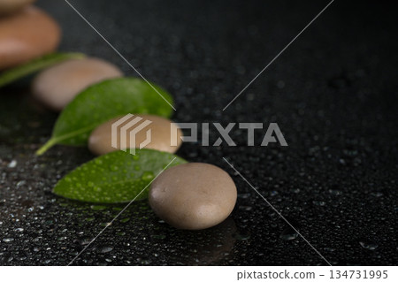 Smooth stones and green leaves with water droplets on black surface Smooth stones and green leaves with water droplets on black surface 134731995