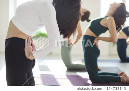 Close-up of women in yoga class doing camel asana, mindful backbend alignment Close-up of women in yoga class doing camel asana, mindful backbend alignment 134732143
