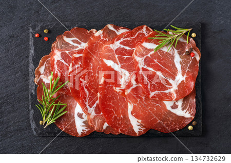 Sliced capicola coppa meat on dark slate board with rosemary 134732629
