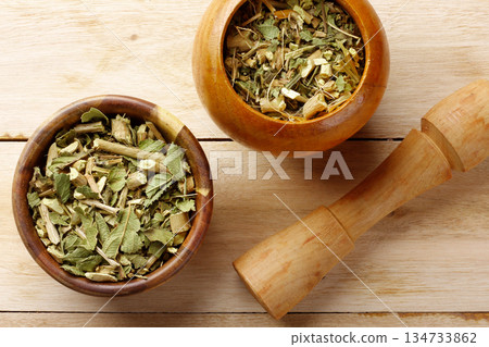 Lemon balm, Melissa officinalis, dried leaves in two wooden bowls with a pestle on a rustic wooden table 134733862