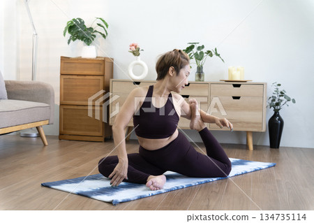 Asian woman in her 50s warms up on a yoga mat on the floor before starting 134735114