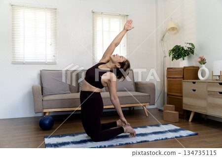 Adult woman 50+ in workout clothes kneeling on a mat and stretching 134735115