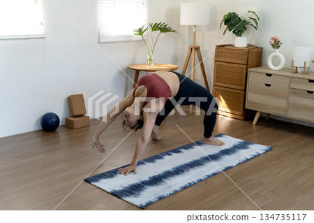 A fifty year old + woman doing yoga poses with her back stretched and her hands 134735117