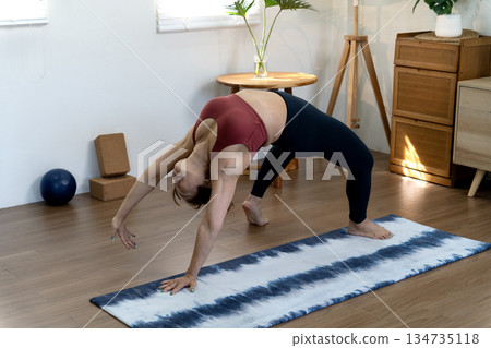 A fifty year old + woman doing yoga poses with her back stretched and her hands 134735118