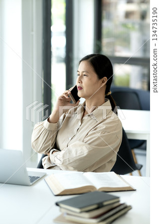 Elder female executive uses a mobile phone to talk at the desk Elder female executive uses a mobile phone to talk at the desk 134735190