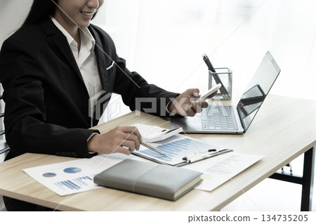 businesswoman Sitting at desk using smartphone and laptop with data from graph 134735205