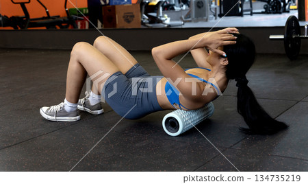 young woman is exercising while lying down using a circular device to roll on the floor 134735219