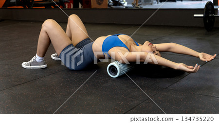 young woman is exercising while lying down using a circular device to roll on the floor 134735220