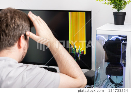 Man reacts with dismay to a broken computer monitor displaying vivid colored lines, representing tech failure, device damage, and user frustration 134735234