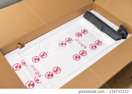 Open cardboard box containing new electronic device parts, featuring protective white foam and plastic bags with safety warnings, illustrating unboxing and product delivery 134735252