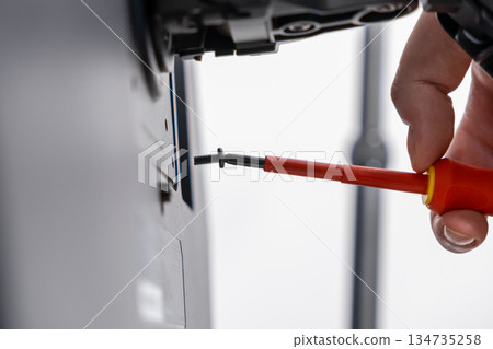 Professional hand uses red insulated screwdriver to fasten black screw into bracket, demonstrating meticulous technical installation, precise assembly, and repair Professional hand uses red insulated screwdriver to fasten black screw into bracket, demonstrating meticulous technical installation, precise assembly, and repair 134735258