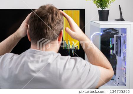Upset man with hands on head seeing a broken computer monitor showing yellow lines, symbolizing a severe tech problem, hardware failure, and repair need Upset man with hands on head seeing a broken computer monitor showing yellow lines, symbolizing a severe tech problem, hardware failure, and repair need 134735265