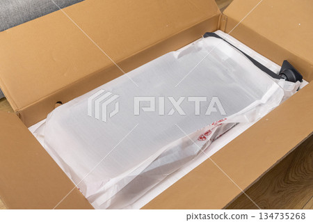 Open cardboard delivery box with new electronic product securely wrapped in protective packaging, representing an exciting unboxing moment from online shopping Open cardboard delivery box with new electronic product securely wrapped in protective packaging, representing an exciting unboxing moment from online shopping 134735268