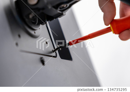 Skilled hand meticulously uses an insulated red screwdriver, fastening a small black screw into a modern device component for assembly and professional technical repair 134735295