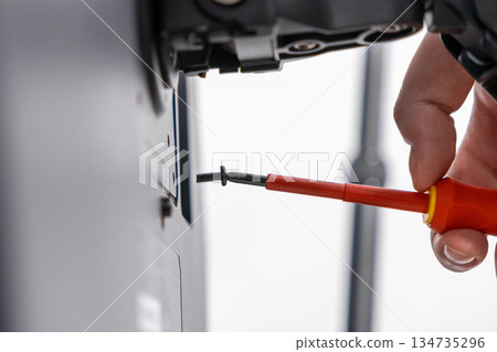 Hand holding an insulated red screwdriver to meticulously fasten a black screw into a technical device, symbolizing precision, repair, and assembly Hand holding an insulated red screwdriver to meticulously fasten a black screw into a technical device, symbolizing precision, repair, and assembly 134735296