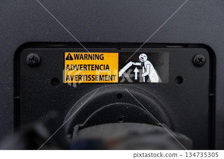 Close-up of yellow warning label with WARNING ADVERTENCIA AVERTISSEMENT text and graphic of person lifting, indicating important safety information for industrial machinery operation 134735305