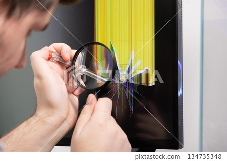 Technician examines broken monitor screen with magnifying glass, diagnosing display damage, representing electronic repair and vital IT support 134735348