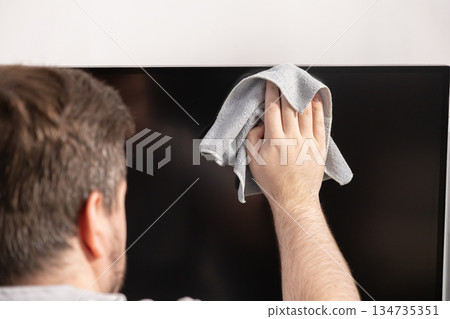 Person's hand diligently wiping a large, dark television screen with soft grey microfiber cloth, promoting home hygiene and electronic device care Person's hand diligently wiping a large, dark television screen with soft grey microfiber cloth, promoting home hygiene and electronic device care 134735351