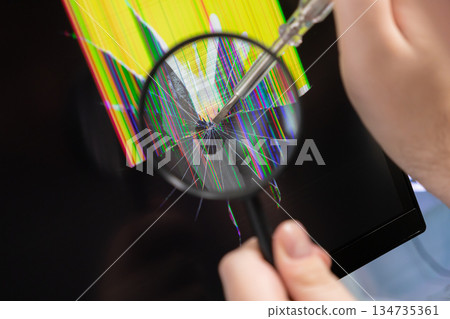 A technician uses a magnifying glass to inspect a severely cracked electronic screen, revealing pixel damage and the intricate process of device repair and diagnostics A technician uses a magnifying glass to inspect a severely cracked electronic screen, revealing pixel damage and the intricate process of device repair and diagnostics 134735361