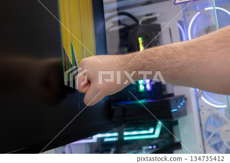 Frustrated gamers fist violently smashes a cracked computer monitor, displaying bright colorful lines, symbolizing technology failure, gaming rage, and digital stress Frustrated gamers fist violently smashes a cracked computer monitor, displaying bright colorful lines, symbolizing technology failure, gaming rage, and digital stress 134735412