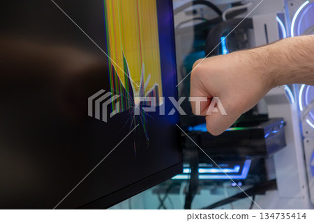 Person's clenched fist near a cracked computer screen displaying colorful lines and spiderweb pattern, depicting technological frustration and digital rage in modern life Person's clenched fist near a cracked computer screen displaying colorful lines and spiderweb pattern, depicting technological frustration and digital rage in modern life 134735414