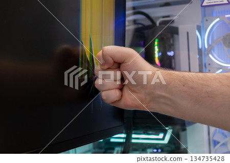 Clenched fist aggressively strikes a computer monitor screen, causing significant pixel damage, representing intense user frustration, anger, and technological breakdown 134735428