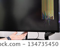 A human hand holds a severely broken computer monitor screen displaying starburst cracks and vibrant colorful lines, illustrating device damage 134735450