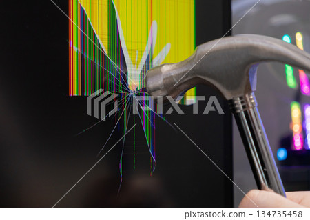 Hammer striking a computer monitor, causing an intensely shattered screen with vibrant colorful pixel lines, representing technology failure, work frustration, or urgent hardware repair 134735458