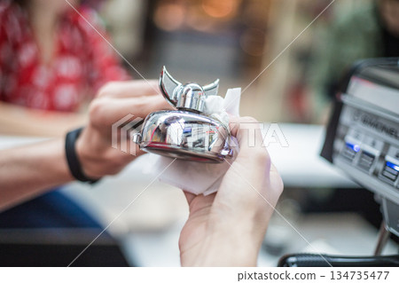Barista wipes a metal bell for orders with a napkin Barista wipes a metal bell for orders with a napkin 134735477