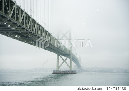 A panoramic view of the Akashi Kaikyo Bridge stretching through a fantastic landscape shrouded in morning mist 134735488