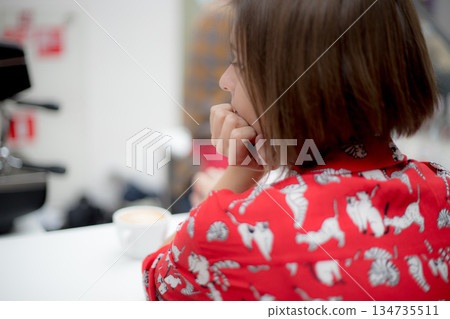 The young girl in red shirt looks away in the background of a shopping cafe. Back view 134735511
