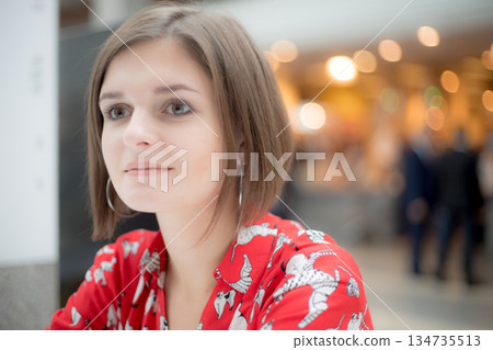 Young women in red shirt looks away on the background of a shopping center 134735513